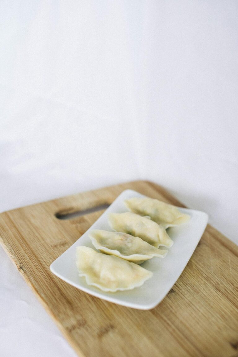 A minimalist close-up of four dumplings on a white plate with a wooden board background.