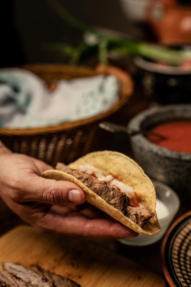 Close-up of a hand holding an authentic Mexican taco with fresh ingredients, highlighting traditional flavors.